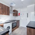Modern kitchen with wooden cabinets, white subway tile backsplash, and stainless appliances including washer, oven, and gas hob on gray countertops.