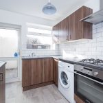 Modern kitchen with dark wood cabinets, white subway tile backsplash, and stainless steel appliances including a washing machine and gas range.