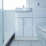 Modern white bathroom vanity with curved sink and chrome faucet beside a glass shower enclosure.