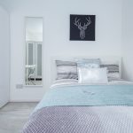 Minimalist white bedroom with a white bed, blue-gray bedding, and a geometric deer head artwork above the headboard.