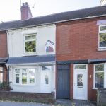 Row of terraced houses; the white-painted middle house has a real-estate sign mounted on the wall above the ground-floor window.