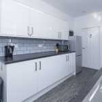 Modern white kitchen with upper and lower cabinets, gray countertop, and subway tile backsplash along a long counter.
