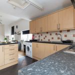 Bright kitchen with light wood cabinets, black countertops, and tiled backsplash; washing machine under the counter near a sink area.