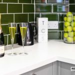 5f299540-2654-4eb7-9a32-79eb0a32002djpg | RENT A ROOM | Professional House Shares in Warwickshire & West Midlands Champagne bottle with two fluted glasses of bubbly on a white countertop, green tile backsplash in the background.