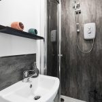 Bathroom vanity with white sink and chrome faucet, black shelf with peach and teal hair dryer bowls above a gray tile backsplash