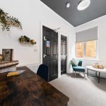 Bright living room corner with dark double doors, white walls, and a wooden desk topped with books; wall-mounted plant shelves above.