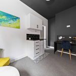Modern home office with white cabinetry, black accent wall, desk, shelves, and colorful artwork on the wall