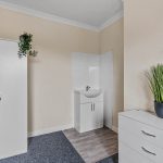 Utility room with white cabinets, a small sink, and a tall green plant on a white dresser against beige walls.