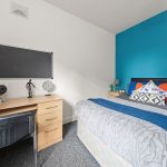 Twin bedroom with a blue accent wall, two beds, and a wooden desk displaying a globe and decorative items.