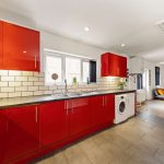Modern kitchen with glossy red cabinets, white subway-tile backsplash, and a double sink along a long counter.