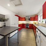 Modern kitchen with red glossy cabinets, white appliances, and a black countertop island.