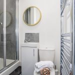 4cb0e074-8167-470b-823e-e0d1167bce66jpg | RENT A ROOM | Professional House Shares in Warwickshire & West Midlands Compact modern bathroom with a glass shower enclosure, round gold-framed mirror, white sink and toilet, and towels on the toilet.