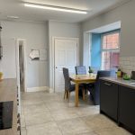 Modern kitchen with gray cabinets, stainless steel appliances, and a wooden dining table with four gray chairs by a windowed wall.