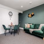 Living room with a green velvet sofa, patterned cushions, and a round wooden coffee table area.