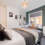 Modern bedroom with white and dark green walls, a neatly made bed, and a wooden dresser by the window.