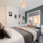 Modern bedroom with white and dark green walls, a neatly made bed, and a wooden dresser by the window.